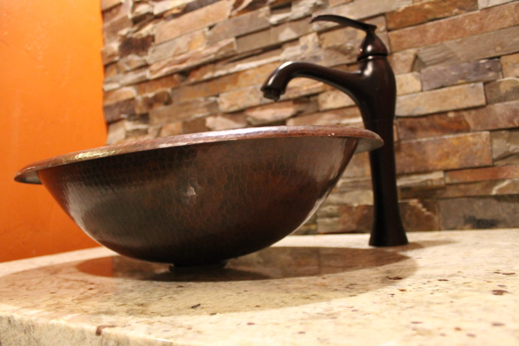 copper vessel sink in powser room with stone wall